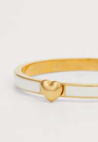 Bracciale a bangle in tonalità oro con un accento a forma di cuore liscio e inserti in smalto bianco, caratterizzato da un design sottile e arrotondato.