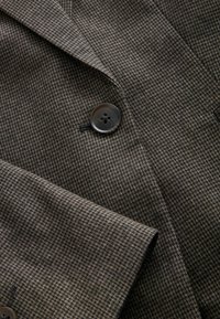 Brązowa marynarka w wzór houndstooth z wykładanym kołnierzem, z ciemnym guzikiem i teksturowanym materiałem, prezentująca dopasowany krój.