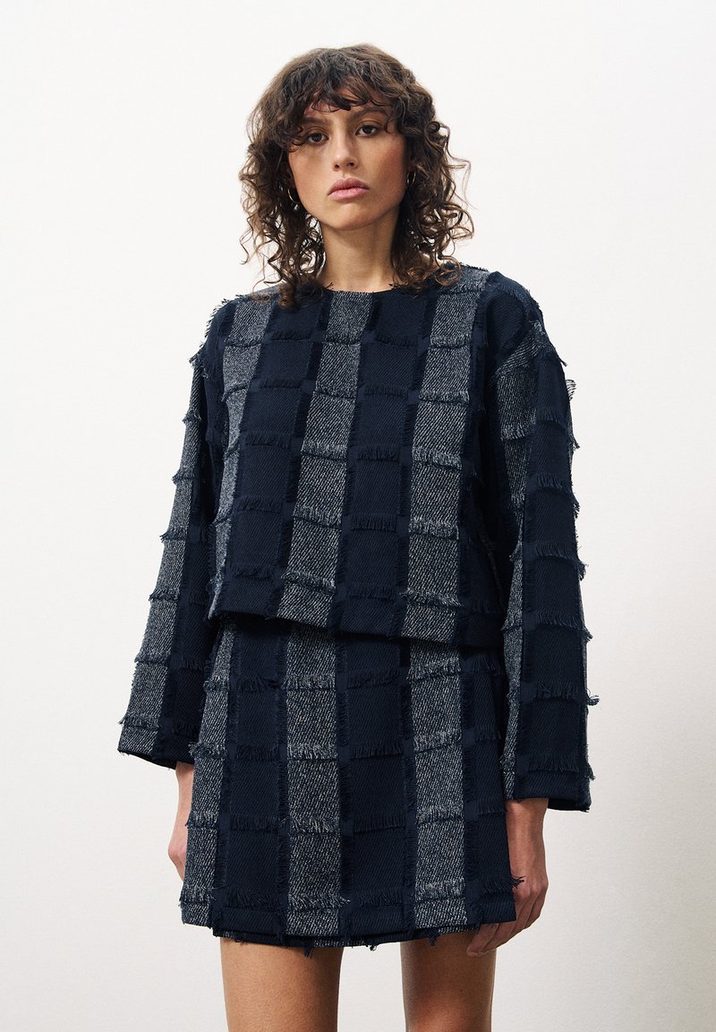 Marineblauwe en grijze geblokte outfit met franjerand, bestaande uit een lange mouw top en een bijpassende mini rok; met een gestructureerde stof.