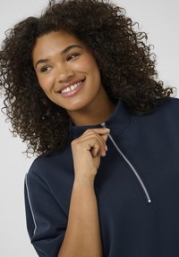 Navy zip-up top with a high collar, short sleeves, and white piping accents. The fabric appears smooth with a subtle texture.