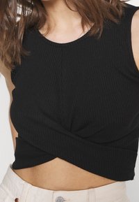 Černý žebrovaný crop top s kulatým výstřihem a zkrouceným předním detailem, vyrobený z elastického materiálu.