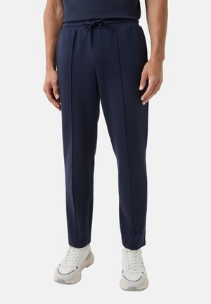 Marineblauwe joggingsbroek van zachte stof, met een trekkoord taille, zijnaad en rechte pijpen. Draagt met witte sneakers.