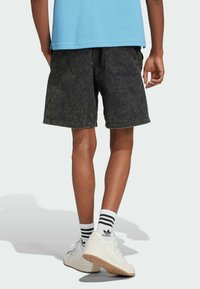 Svarta denimshorts med en urtvättad, texturerad yta, med en bakficka. Kombinerat med vita sneakers och randiga strumpor.