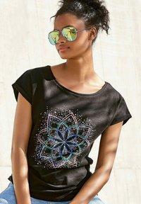 Camiseta negra de manga corta con mangas enrolladas, que presenta un diseño de mandala colorido con acentos en azul, rosa y blanco, sobre un fondo liso.