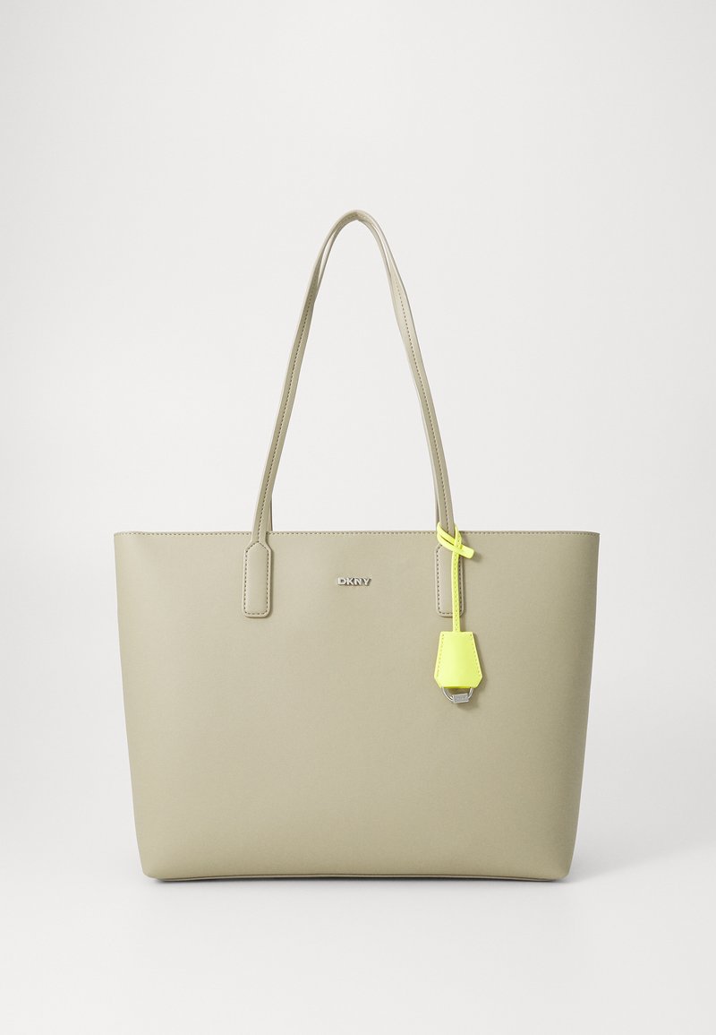 Beige laukku olalla, jossa on kaksoiskahvat, sileä pinta ja keltainen korostetagi. "DKNY"-logo näkyy selvästi edessä.