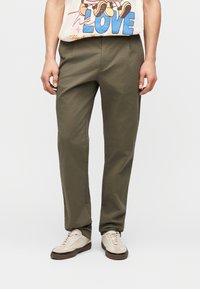 Άνδρας που φοράει χακί παντελόνι κανονικής γραμμής, μπεζ αθλητικά παπούτσια και μπλουζάκι με σχέδιο καρτούν και το κείμενο "LOVE", το οποίο έχει μπει μέσα στο παντελόνι.