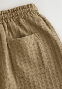 Beige elastic-waist pants featuring a vertical ribbed texture and a single back pocket with a stitched outline. Soft fabric.