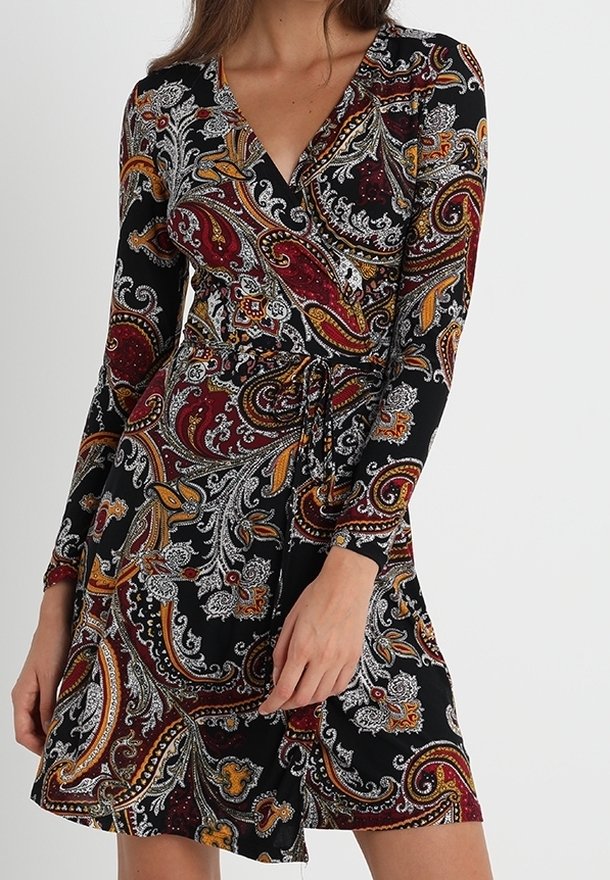 Femme portant une robe portefeuille à manches longues, longueur genou, avec une base noire et un motif cachemire complexe en rouge, or et blanc.