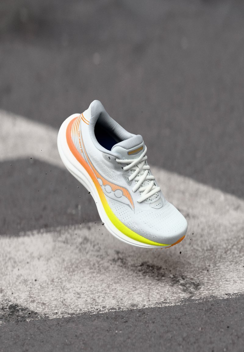 Lekki but biegowy charakteryzuje się szarym siateczkowym wierzchem z pomarańczowymi i żółtymi akcentami, amortyzującą podeszwą oraz teksturowanym noskiem.