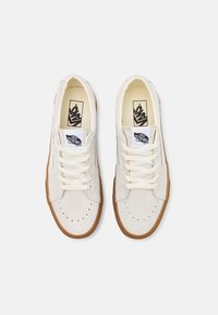 Cremefarbene Wildledersneaker mit perforierter Kappe, cremefarbenen Schnürsenkeln und einer Gummisohle. Mit Vans-Logo auf der Zunge.