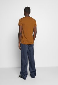 Brun kortärmad t-shirt gjord av bomull, i kombination med löst sittande marinblå byxor. Tyget verkar slätt utan synliga mönster eller detaljer.