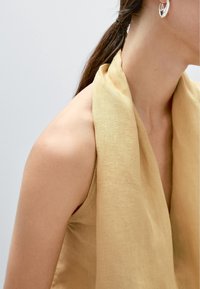 Top en lin jaune clair avec un design croisé décontracté. Doté d'un décolleté en V profond et d'une large ouverture au niveau du cou, mettant en valeur l'épaule. Texture simple.
