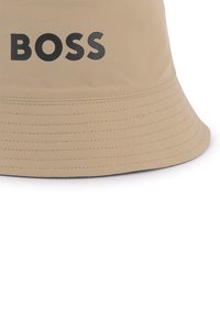 Chapeau seau beige à large bord, fabriqué en tissu lisse, avec le logo noir "BOSS" à l'avant et des détails de couture contrastants.