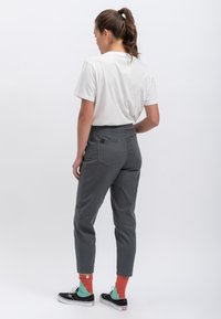 Grijze taps toelopende broek met zakken, hoge taille en stikdetails. Gecombineerd met een wit T-shirt en kleurrijke sokken, gedragen met zwarte sneakers.