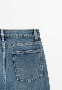 Jeans in denim di colore blu medio, taglio dritto, cinque tasche e dettagli di cucitura visibili. Il tessuto ha una superficie liscia e leggermente strutturata.