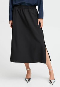 Jupe noire mi-longue avec une taille élastique, fente latérale et texture lisse. Associée à des talons métalliques à bouts pointus.