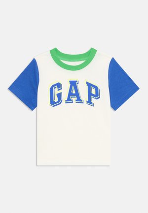 Lyhythelmainen T-paita, jossa on valkoinen vartalo, siniset hihat, vihreä kaulus ja "GAP"-logo paksuilla sinisillä ja keltaisilla kirjaimilla.