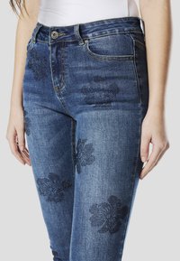 Donkere blauwe denim jeans met een slim fit, voorzien van bloemmotieven en zakken. Het materiaal heeft een lichte textuur en een gedragen uitstraling.