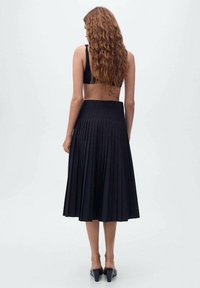 Gonna midi plissettata nera con vita alta, texture liscia e design fluido. Materiale lucido che riflette leggermente la luce.