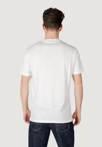Camiseta de algodón blanca con cuello redondo clásico y mangas cortas, mostrada desde la parte de atrás, combinada con jeans de mezclilla oscura.