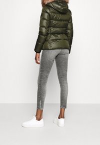 Olivgrön dunjacka med huva av fejkpäls, kombinerad med figurnära grå jeans och vita sneakers. Texturerat tyg och stilren design.