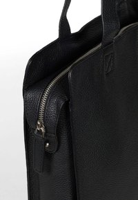 Czarna skórzana torba o teksturowanym wykończeniu, z srebrnym zamkiem błyskawicznym, dwoma mocnymi uchwytami i prostokątnym kształtem.