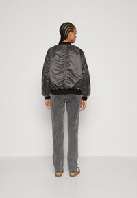 Giacca bomber nera con un leggero lucido, colletto e polsini a costine, vestibilità comoda. Indossata con jeans grigi e calzature con motivo.