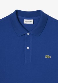 Granatowa koszulka polo z trzema guzikami, z zielonym logo krokodyla na lewej piersi, teksturowany materiał.