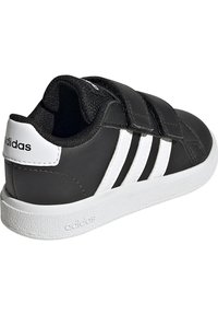 Baskets noires avec trois bandes blanches et des accents. Sangles Velcro, dessus en synthétique texturé et semelle en caoutchouc. À l'arrière se trouve le logo de la marque.