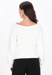 Pulover alb tricotat cu un decolteu larg tip barcă și mâneci lungi. Are un model texturat și o tăietură scurtă la tiv.