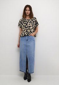 Black floral blouse with short sleeves, paired with a light blue denim maxi skirt featuring a front slit and raw hem, complemented by black ankle boots.