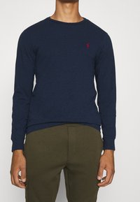 Mörkblå långärmad T-shirt i bomull med rund halsringning och en liten röd logotyp på bröstet. Mjuk textur och figursydd design.