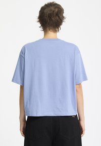 T-shirt a maniche corte di colore azzurro chiaro con scollo rotondo, vestibilità rilassata e orlo dritto. Il tessuto sembra morbido con cuciture minime, indossato con pantaloni neri.