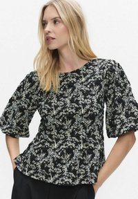 Svart blus med blommönster som har rund halsringning, puffade korta ärmar och ett strukturerat tyg med vita och gröna botaniska mönster.