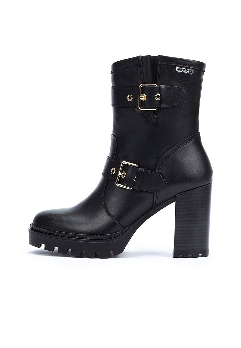 Botas de tobillo de cuero negro con un tacón alto y grueso, que presentan dos correas ajustables con hebillas doradas y una suela de goma texturizada.