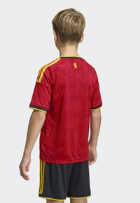 Röd sporttröja med gula detaljer och svart kantning, med ett strukturerat flammmönster och en logotyp på övre ryggen. Svarta shorts med gula ränder.