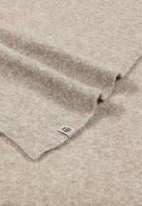 Light beige woolen blanket with a soft, textured surface. Features a folded edge and a small woven label in the corner.