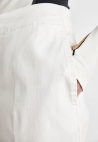Hvit bomullsstoff har en fremtredende sidelomme med en strukturert design. Teksturen ser jevn ut uten synlige mønstre.