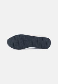 Suola di sneaker caratterizzata da un motivo in gomma testurizzata, colore blu scuro e una leggera curvatura nella punta. Bordo rinforzato per una maggiore durata.