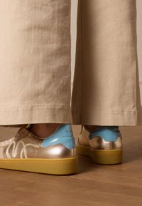 Gouden en blauwe sneakers met een gestructureerde, gele zool. Heeft een gladde metallic afwerking en ingewikkelde ontwerpdetails aan de zijkanten.