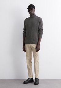 Grau gestreifter Rollkragenpullover, cremefarbene Hose und schwarze Knöchelstiefel. Das Outfit zeichnet sich durch ein minimalistisches Design ohne zusätzliche Muster aus.