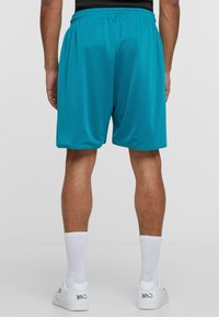 Turkisbåndede treningsshorts med mesh-textur, elastisk midjebånd og løs passform. Brukt med hvite sneakers og hvite sokker i ankel-lengde.