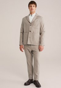 Sivi šalni blazer s reverjem, ki ima dve sprednji žep in gumbasto zapiranje, v kombinaciji s ožjimi hlačami in temnimi čevlji.