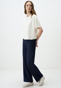 Wit t-shirt met korte mouwen in combinatie met marineblauwe wijde broek en witte sneakers. Soepele stof, relaxte pasvorm, eenvoudig ontwerp en neutrale kleuren.