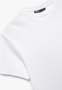 Witte katoenen T-shirt met een geribde ronde hals, korte mouwen en een zachte textuur. Bevat een label met de tekst "Køtten Basic" aan de binnenkant van de halslijn.