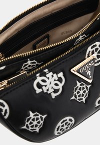 Musta synteettinen käsilaukku, jossa on valkoisia brändilogojaja, kultaisia yksityiskohtia ja vetoketjukiinnitys. Sisäpuoli on beige, ja siinä on vetoketju- ja liukuveneitä.