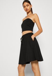 Svart to-delt antrekk med en strapless crop-top og et utsvingt skjørt med elastisk midje og sidelommer. Glatt stoffstruktur.