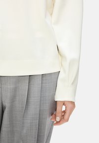  Weißer Sweatshirt mit glatter Textur, ausgestattet mit einem gerippten Saum und Bündchen; kombiniert mit hellgrauen, plissierten Hosen in einem dezenten Karomuster.