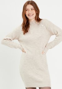 Vestido de suéter beige acanalado con un cuello alto, mangas largas y botones decorativos en el hombro. Textura suave y diseño ajustado.