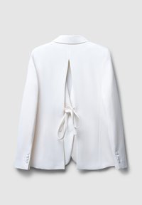 Blazer bianco su misura con un'apertura sul retro e dettaglio a cravatta. Maniche lunghe con accenti di bottoni, texture liscia e design strutturato.